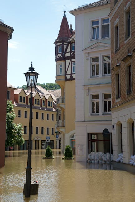 The image depicts a street scene with a row of multi-storey residential buildings, featuring a mix of cream, beige, and light brown facades with detailed window frames and decorative finishes. The bui